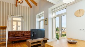 Un salon avec un plancher en bois, un canapé en cuir marron, un téléviseur posé sur un meuble en bois et une table à manger avec un saladier.