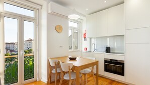 Une cuisine moderne avec des meubles blancs, une table à manger en bois et une vue sur la ville grâce à de grandes fenêtres.