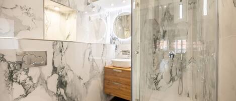 A modern bathroom with marble walls, a glass-enclosed shower, and a wooden vanity.