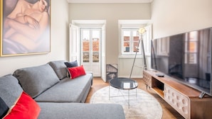 A modern living room with a grey sofa, a large flat-screen TV, and a painting on the wall. - Bairro Alto Prime Duplex by Homing (Lisbon)