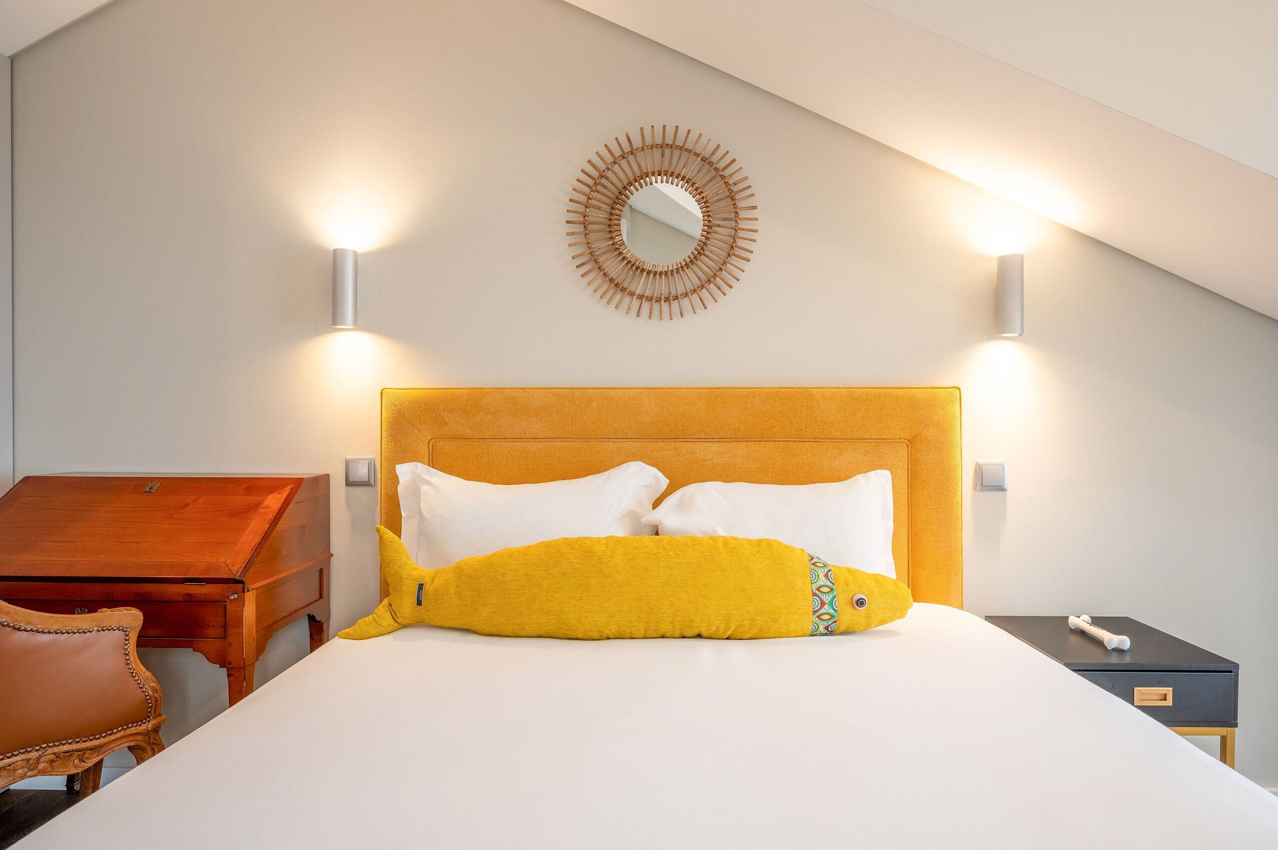 A hotel room with a bed, a wooden nightstand, a small table, and a chair.