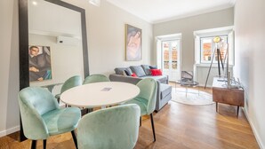 A modern living room with a round table, two green armchairs, a grey sofa with red cushions, a large mirror, and a painting on the wall. - Bairro Alto Prime Duplex by Homing (Lisbon)