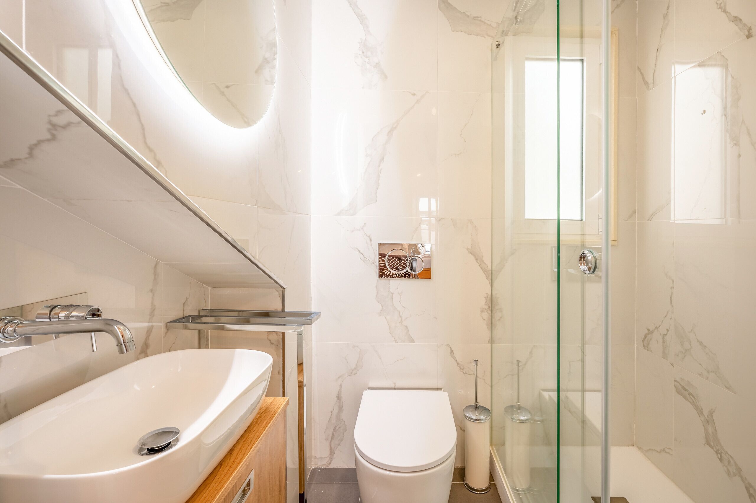 Un baño moderno con lavamanos de mármol, inodoro y cabina de ducha de vidrio.
