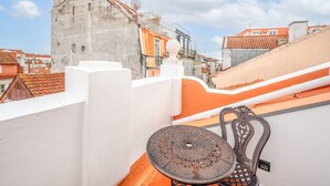 A rooftop terrace with a decorative metal table and chair, a white wall, and a view of colorful buildings in the background. - Bairro Alto Prime Duplex by Homing (Lisbon)