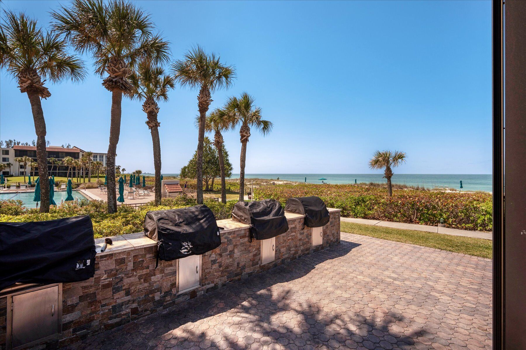 A patio with barbecue grills, palm trees, and a view of the ocean.