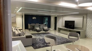 A modern living room with a sofa, chairs, a TV, and a dining area.