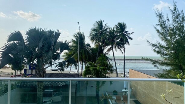 A balcony with a view of the beach, palm trees, and a clear sky.
