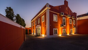 A red building with multiple windows and air conditioning units, surrounded by a paved area.