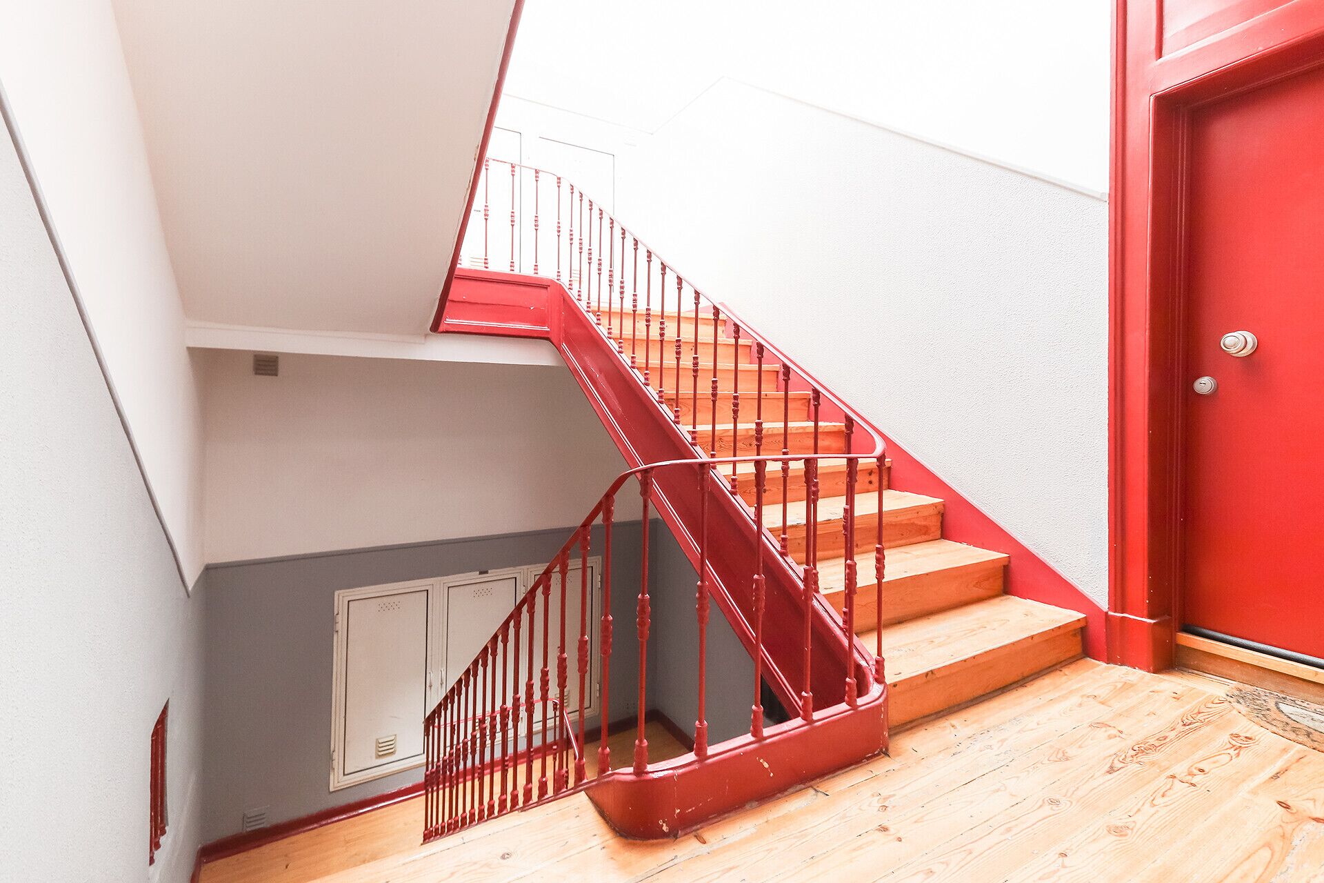 A staircase with red railings leading to a landing, a red door, and a light-colored wall.