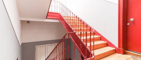 A staircase with red railings leading to a landing, a red door, and a light-colored wall.