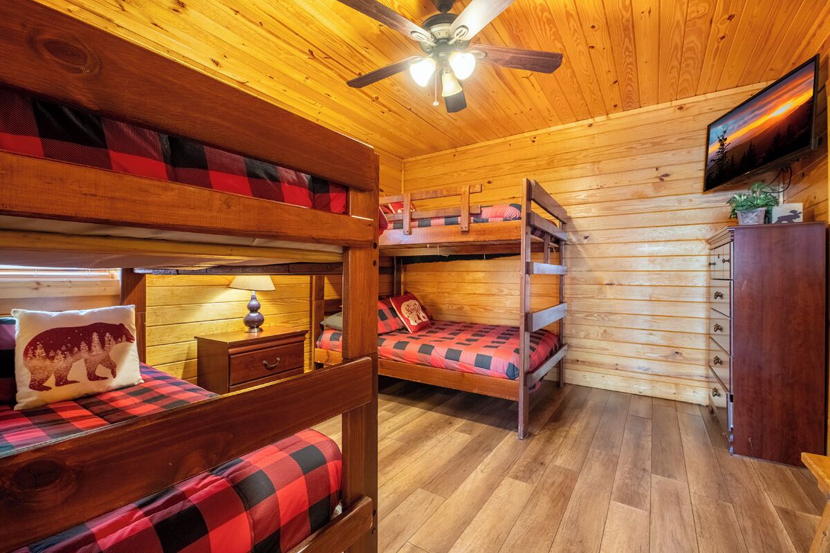 Eine Holzhütte mit Etagenbetten, Holzwänden, einem Deckenventilator und einem an der Wand montierten Fernseher.