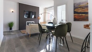 Un moderno comedor con una mesa de vidrio y sillas negras, un sofá, un televisor de pantalla plana y un cuadro abstracto grande en la pared.