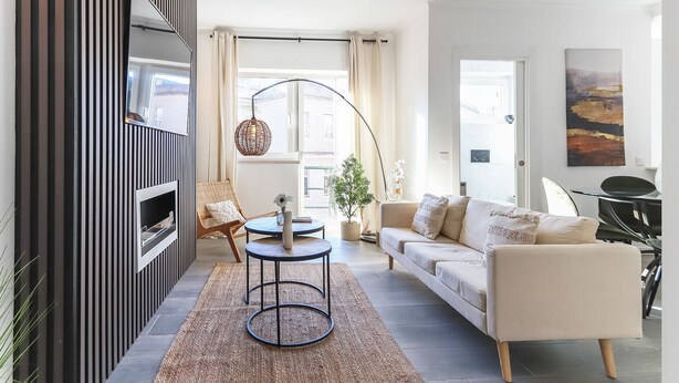 Una sala moderna con un sofá, una mesita redonda, un sillón de mimbre y una lámpara de pie.