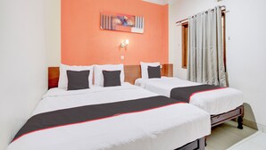 Een hotelkamer met twee bedden, een schilderij aan de muur, een plafondventilator en een raam met gordijnen.