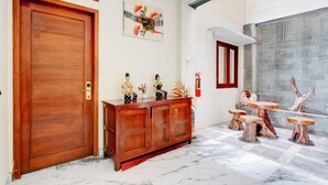 Een houten deur met een nummerbord, een houten kast met decoratieve voorwerpen en een zithoek met een bijzondere tafel en stoelen van een boomstronk.