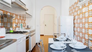 A modern kitchen with white cabinets, a gas stove, and a dining area set for four with white plates and glasses. - Roman Style II near San Pietro - 10 minutes from Vatican and St Peter's Basilica (Roma)