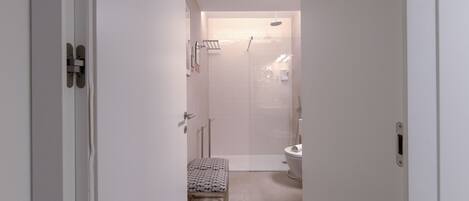 A narrow hallway leading to a bathroom with a shower, toilet, and a bench.