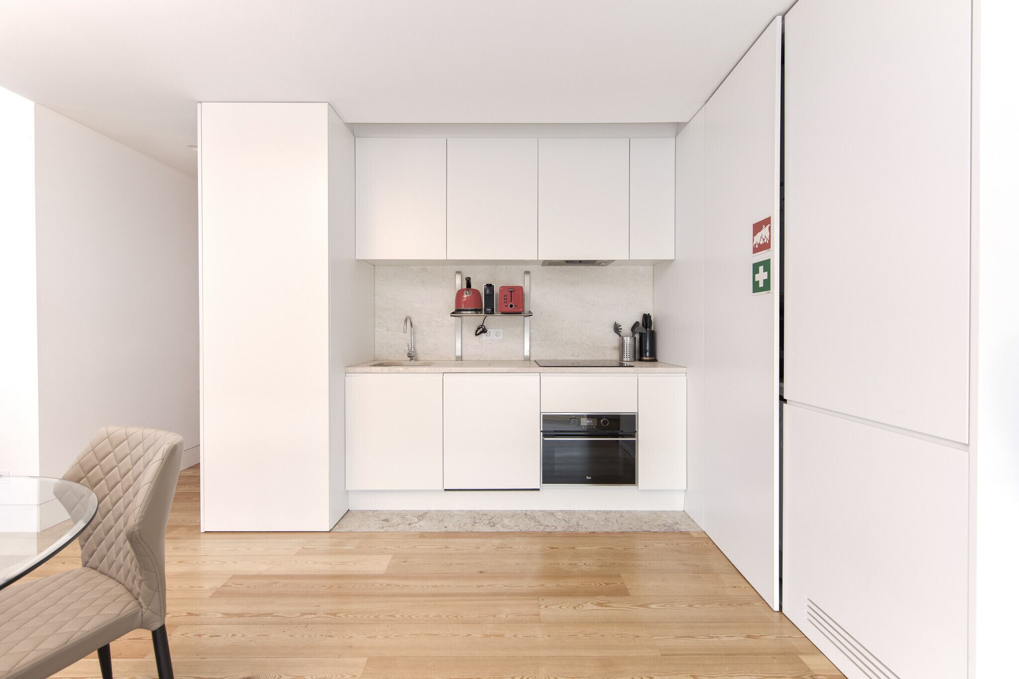 A modern kitchen with white cabinetry, a built-in oven, and a coffee machine.