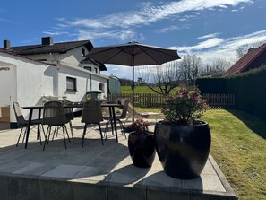 A patio with outdoor furniture, a large umbrella, and potted plants.