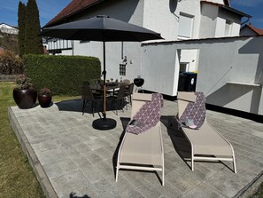 An outdoor patio with a dining table, chairs, and lounge chairs under a large umbrella.