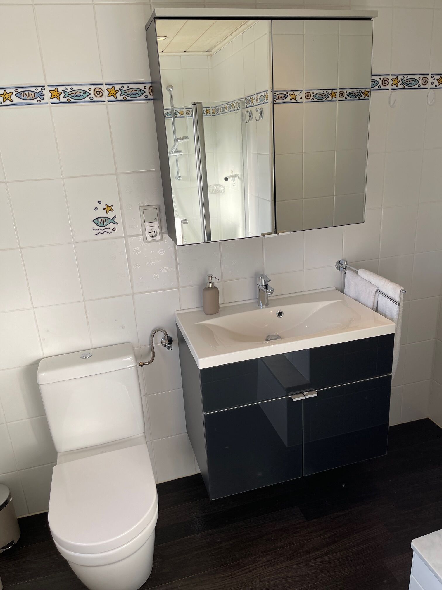 A bathroom with a white toilet, a black vanity with a mirror above, and a white sink.