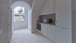 Μια σύγχρονη κουζίνα με λευκά ντουλάπια, φούρνο μικροκυμάτων και φούρνο. Υπάρχει ένα παράθυρο που παρέχει φυσικό φως και προσφέρει θέα προς το εξωτερικό.