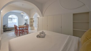 Ένα σύγχρονο δωμάτιο ξενοδοχείου με ένα μεγάλο κρεβάτι, ένα τραπέζι φαγητού με καρέκλες και μια εντοιχισμένη ντουλάπα.