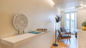 Una sala moderna con una consola blanca, un adorno en la pared, una lámpara de pie y una zona de estar con un sillón y un sofá.