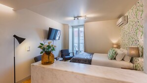 Una habitación de hotel moderna con un mostrador de recepción de mármol, un televisor de pantalla plana en la pared, una cama sofá, una silla y una mesita.