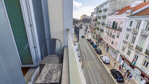 Un balcón con una mesa de madera, una silla de metal y vistas a la calle con coches y edificios.