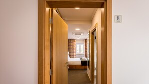 A hotel hallway leading to a room with a bed, a window with curtains, and a sign indicating room number 8.
