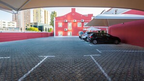 A covered parking area with a red building in the background, a few cars parked, and a clear view of the surrounding cityscape.