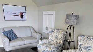 Un salón con un sofá gris, un sillón estampado, una mesa de centro oscura y una lámpara de pie.