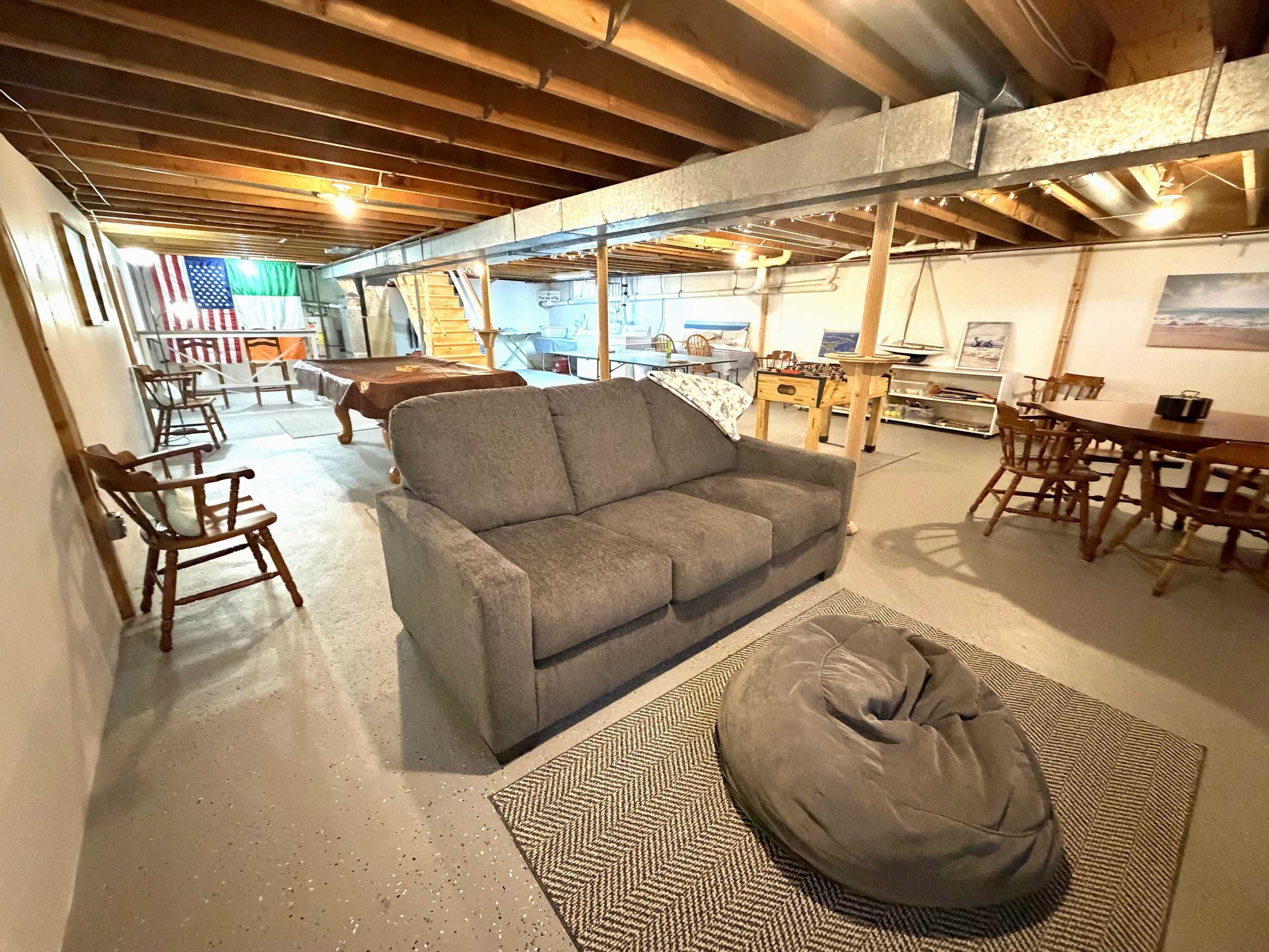 A spacious room with a gray sofa, wooden chairs, a dining table, and a bean bag.