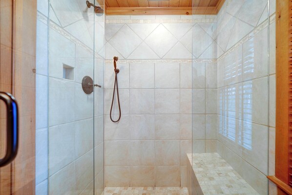 Shower area features a handheld showerhead, shelf, and a bench.