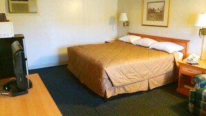 A hotel room with a bed, a desk with a computer, a lamp, and a picture on the wall.