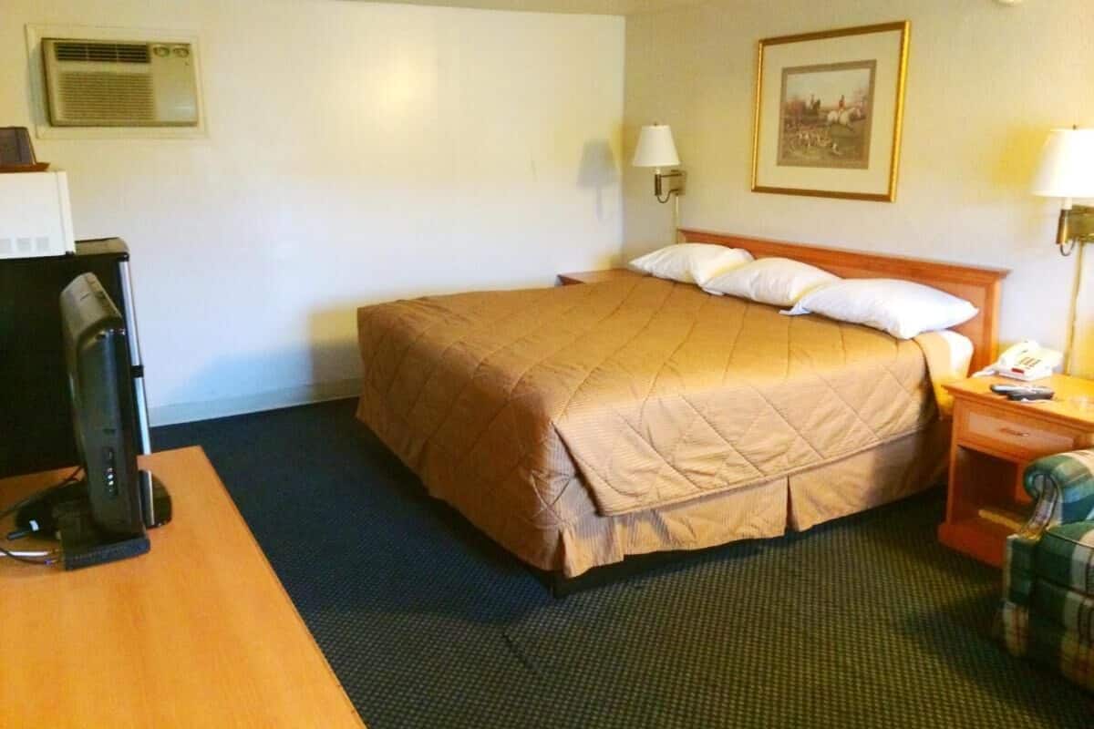 Ein Hotelzimmer mit einem Bett, einem Schreibtisch mit Computer, einer Lampe und einem Bild an der Wand.