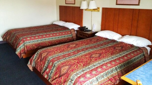 A hotel room with two beds, each with patterned bedding, a nightstand with a lamp, and a framed picture on the wall.