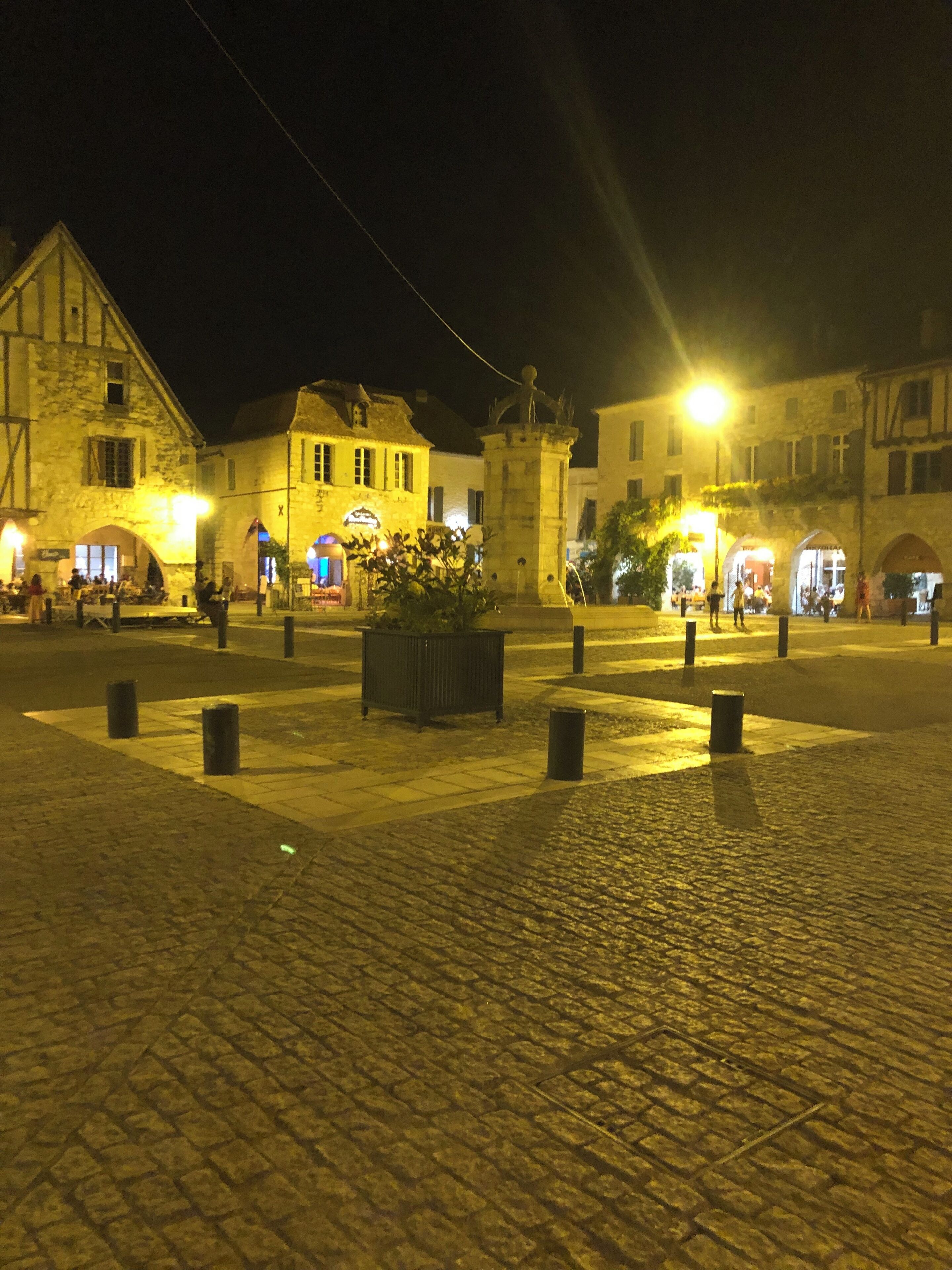 Une place historique, pavée de pierres, bordée de bâtiments en pierre et agrémentée d’une fontaine centrale.