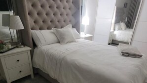 A neatly made bed with white linens, a tufted headboard, and a bedside table with a lamp and a small decorative item. - 3 Bedroom, Sleeps 6, Free Parking (Glasgow)