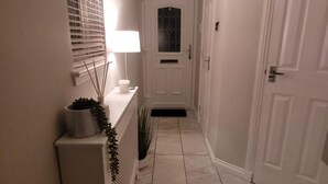 A hallway with a white door, a lit lamp, and a potted plant. - 3 Bedroom, Sleeps 6, Free Parking (Glasgow)