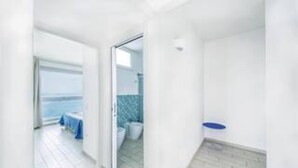 Una habitación luminosa y blanca con vistas al mar a través de una puerta abierta.