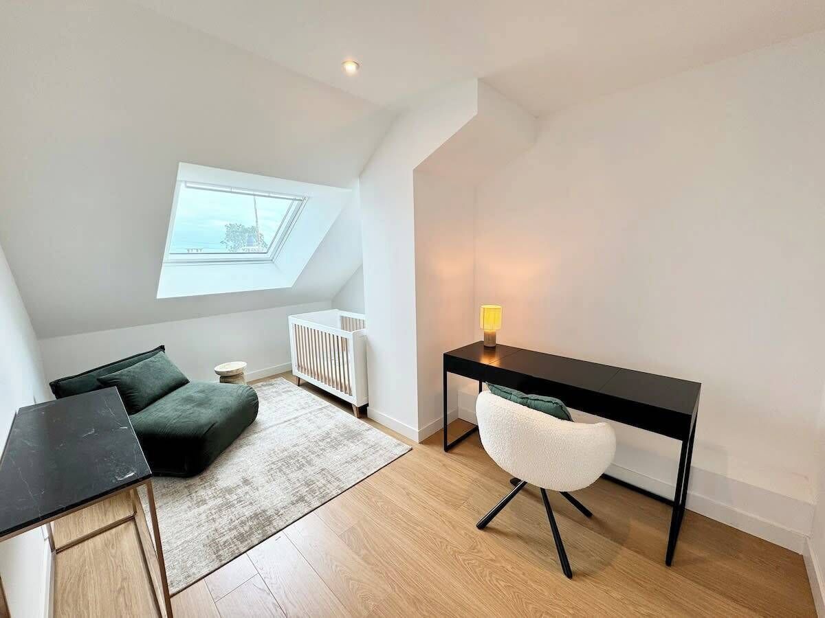 A modern loft bedroom with a skylight, a desk, a chair, a sofa, and a radiator.