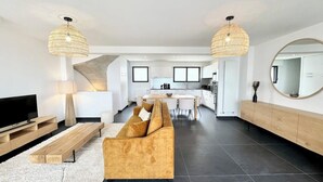 A modern living room with a sofa, TV, and wooden coffee table. There is a kitchen in the background with a dining area. - Villa d’architecte contemporaine - Vue mer 180° (Larmor-Plage)