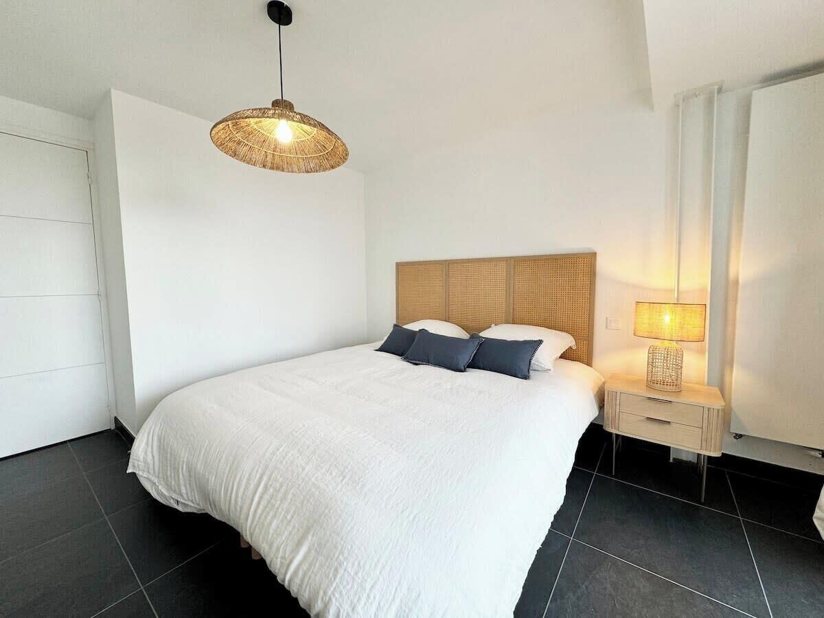 Een slaapkamer met een groot bed, een nachtkastje met een lamp en een hangende lamp.
