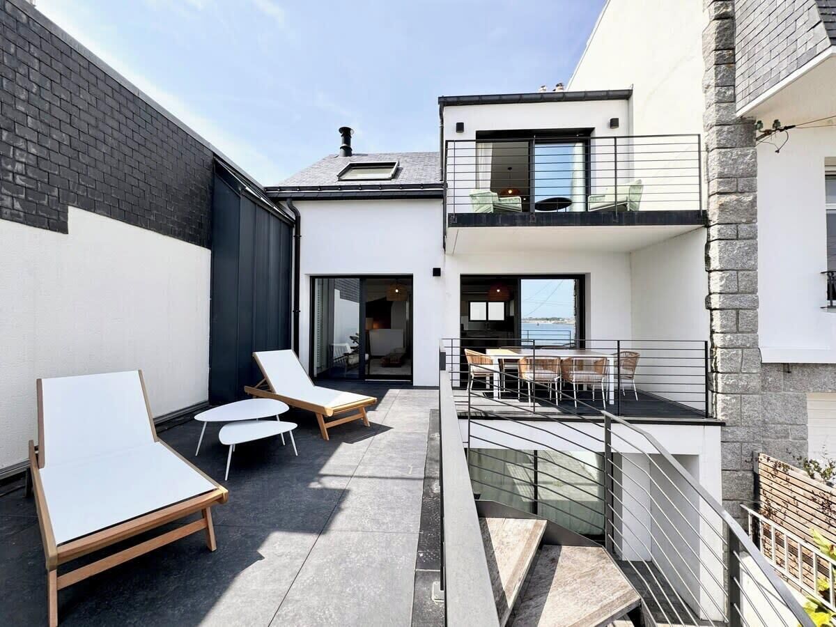 Un patio esterno moderno con poltrone relax, un'area pranzo e vista sul mare.