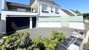 Una casa moderna de dos pisos con garaje, un portón verde y un camino de entrada pavimentado.