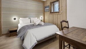 Ein Schlafzimmer mit Holz Kopfteil, einem Bett mit weißer Bettwäsche, einem kleinen Nachttisch, einem Holzstuhl und einem Fenster mit Blick auf Bäume.