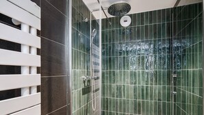 Eine gläserne Dusche mit Regendusche, einem weißen Handtuchhalter und grünen Fliesenwänden.