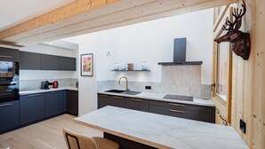 A modern kitchen with a marble countertop, dark cabinets, and a wooden ceiling.